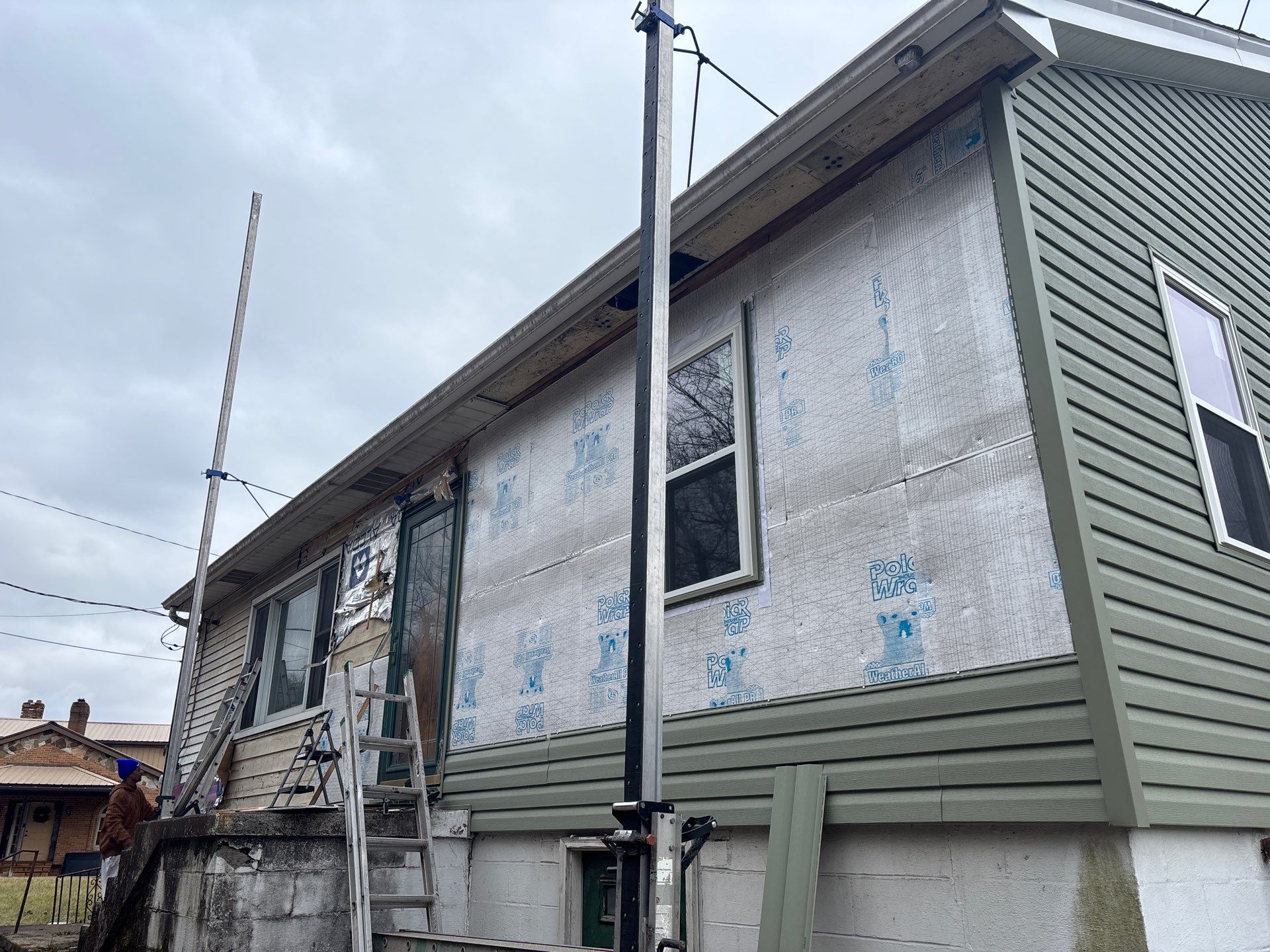 Siding installation in progress on a residential home, showcasing new vinyl siding and protective underlayment, with a ladder and equipment visible.