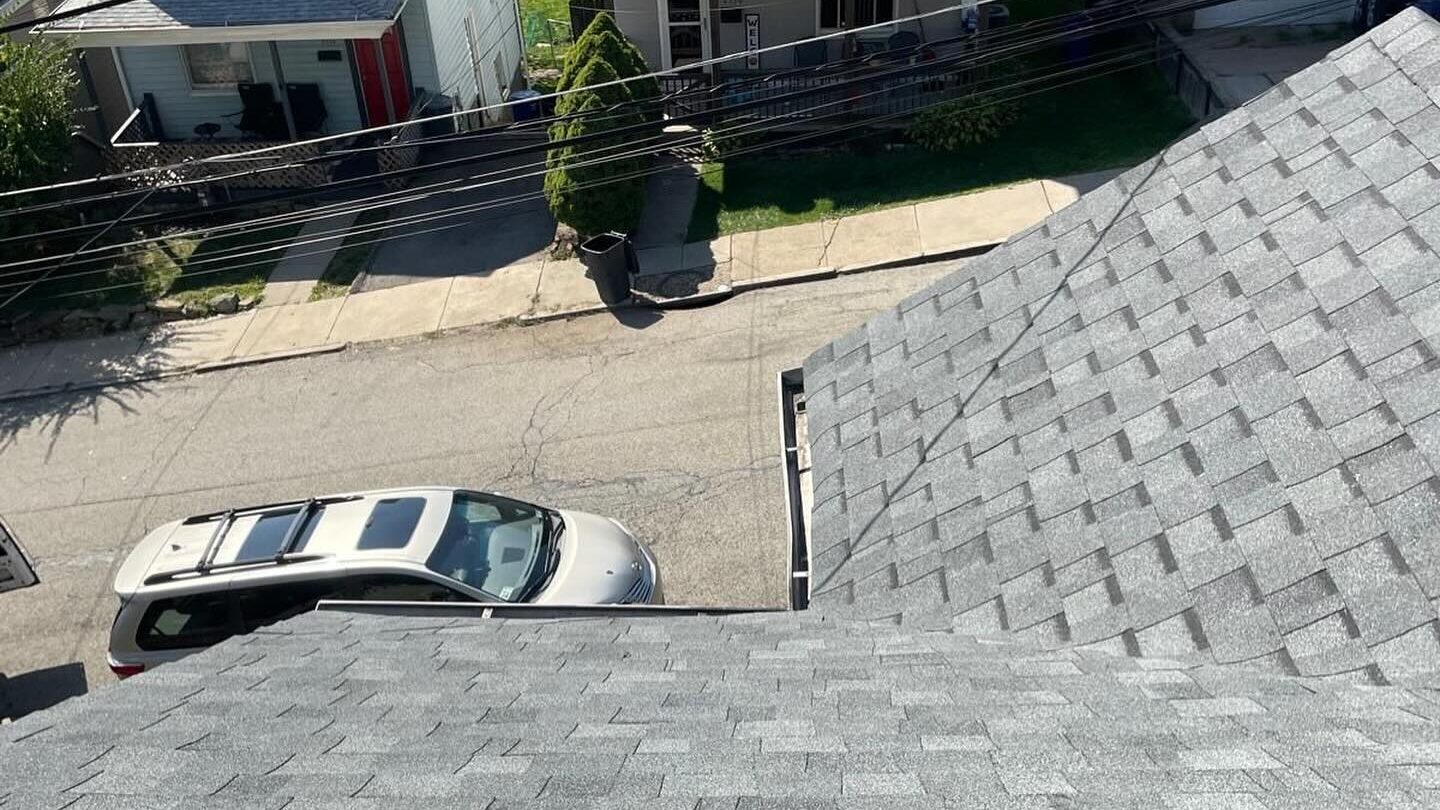 Roof view showcasing new asphalt shingles with a parked vehicle on a residential street, highlighting the quality of Alan Construction's roofing services.