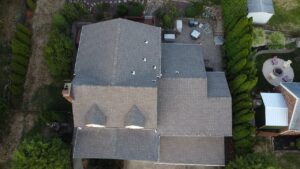 Aerial view of a residential roof with shingles, showcasing a Spanish-style home in Pittsburgh, surrounded by greenery and outdoor furniture.