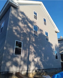 Newly installed gray vinyl siding on a residential home in Robinson Township, featuring multiple windows and shadows cast by nearby trees, showcasing exterior improvements for enhanced curb appeal.