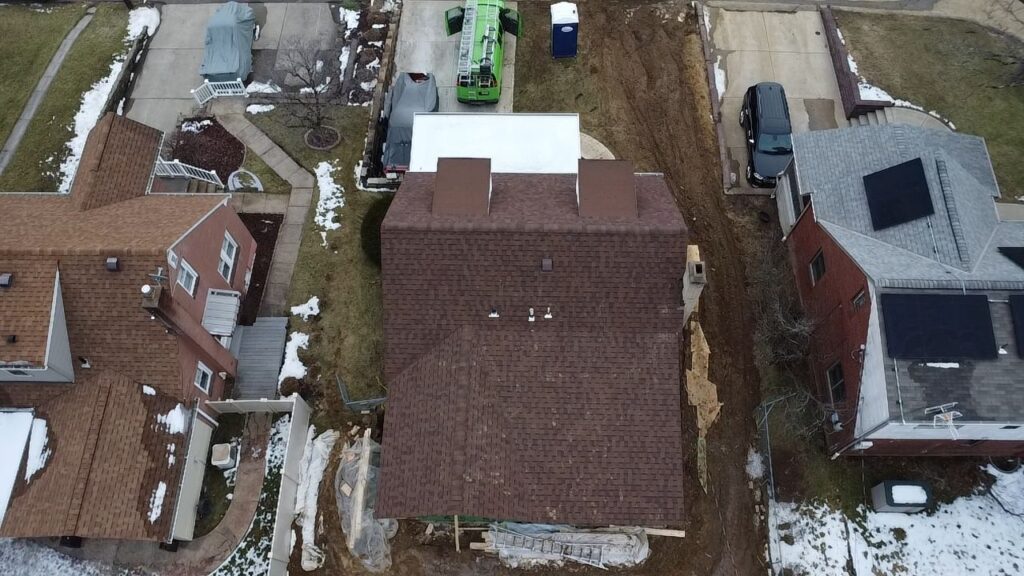 Aerial view of a split-level home in Pittsburgh, showcasing a new roof installation with brown shingles, surrounded by residential properties and construction equipment.
