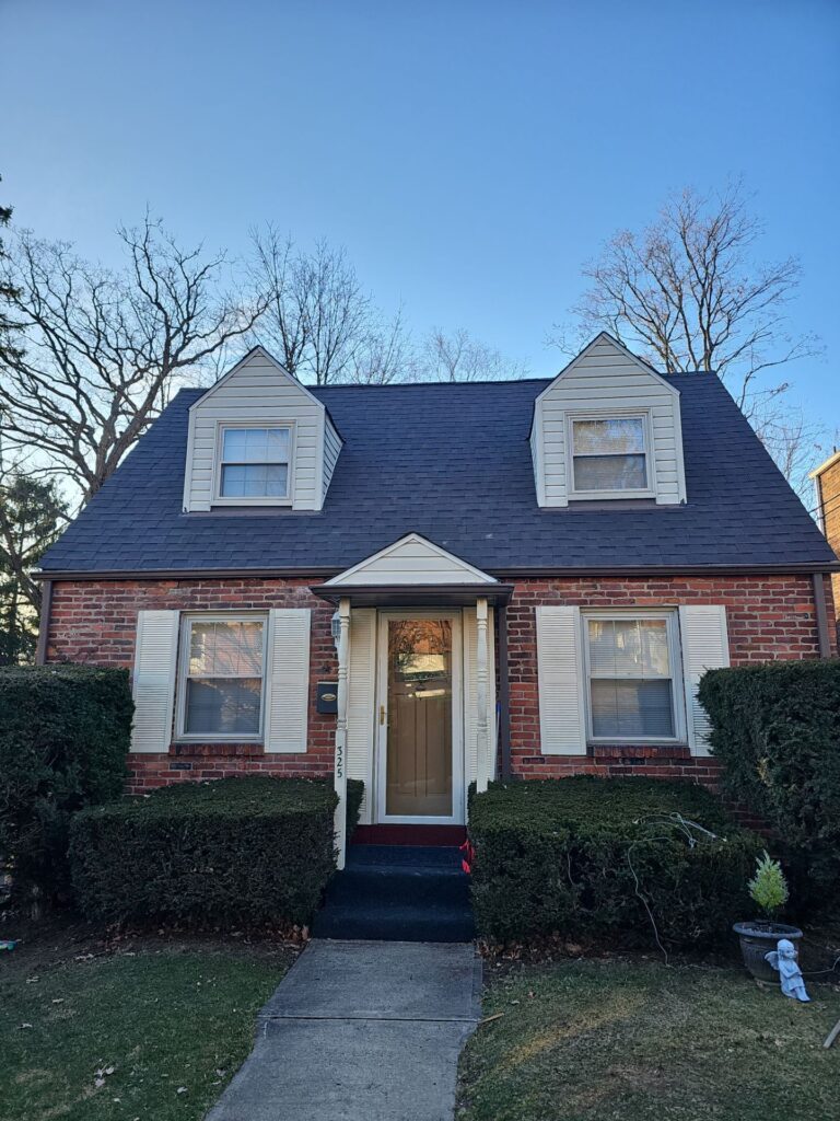 Brick home with a newly installed dark shingle roof, featuring dormer windows and trimmed hedges in a residential setting, relevant to roofing and maintenance discussions for homeowners in Pittsburgh.