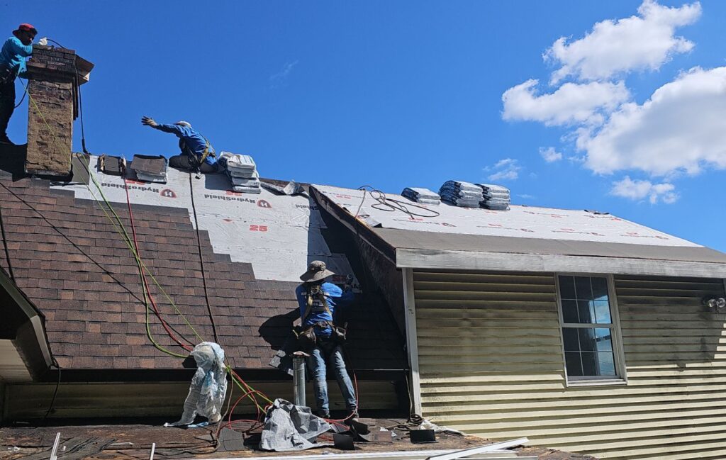 Roofing professionals working on a residential roof in Pittsburgh, applying roofing materials and ensuring safety during installation under a clear blue sky.