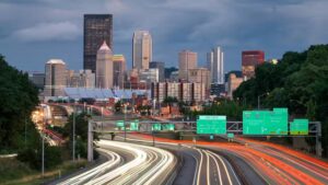 Pittsburgh skyline with highways and light trails, highlighting urban architecture and traffic near residential areas.