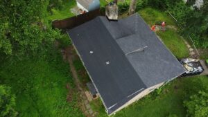 Aerial view of a flat rubber roof on a residential home in Pittsburgh, surrounded by greenery, showcasing roofing installation work.