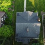 Aerial view of a residential home with a dark shingle roof surrounded by greenery, highlighting the importance of roof maintenance in Wexford, PA.
