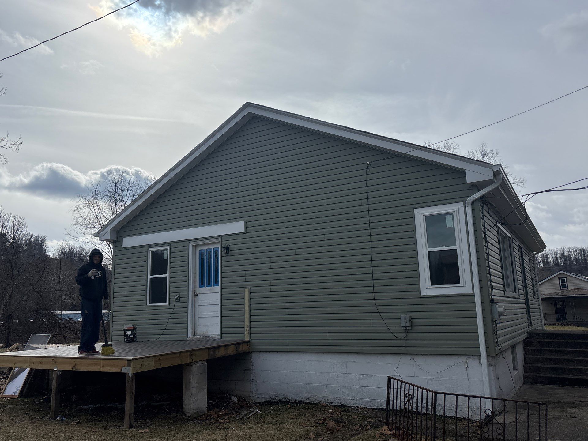 Home exterior with new vinyl siding installation, showcasing a modern appearance and enhanced protection, featuring a person standing on a wooden deck.