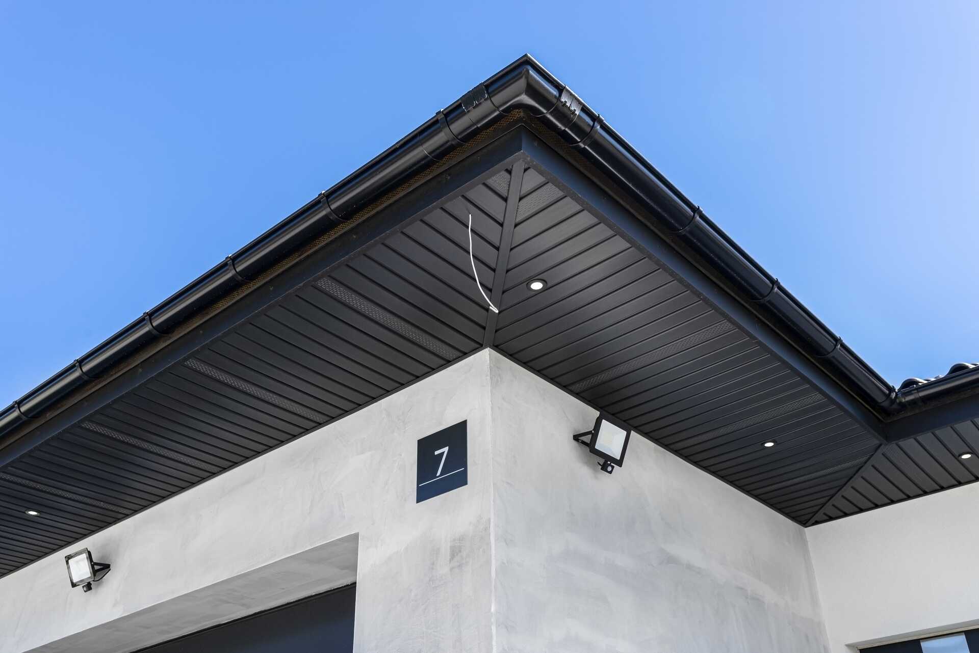 Modern black herringbone soffit and fascia installation with recessed lighting, showcasing attention to detail in exterior design at a residential property.