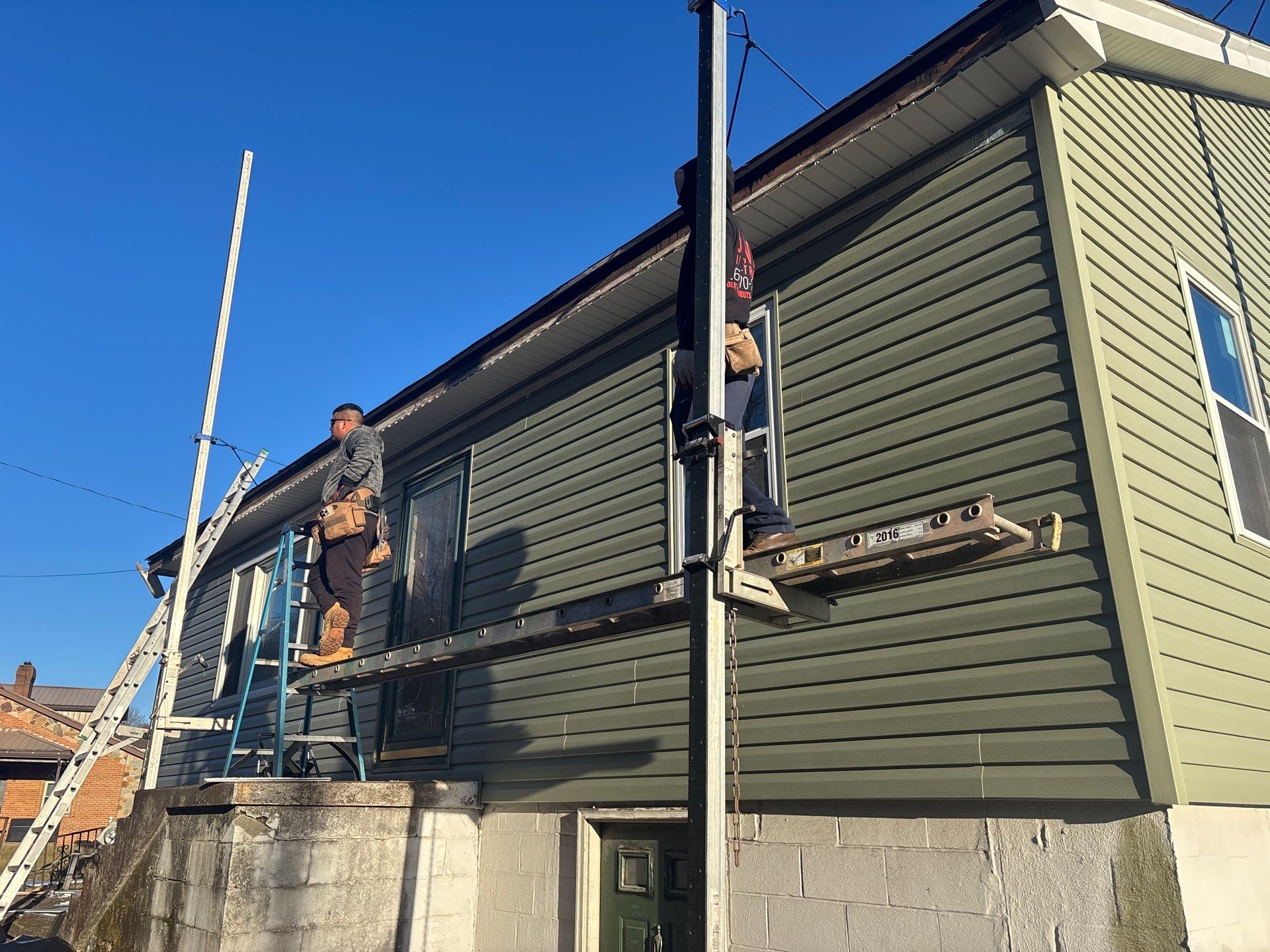 Worker installing vinyl siding on a home, using a ladder and scaffolding, showcasing professional siding installation services by Alan Construction in Pittsburgh.