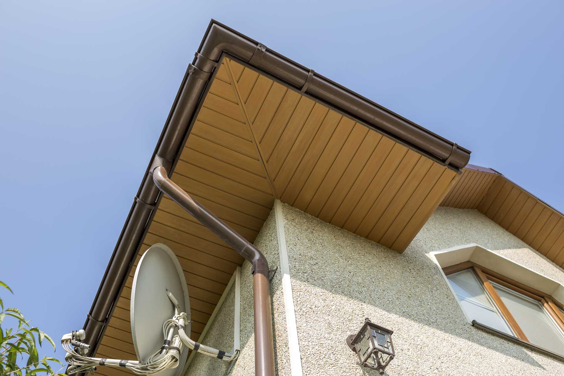 Bottom view of a modern house showing soffit and fascia installation, with a satellite dish and downspout, highlighting essential roofing components for moisture protection and ventilation.