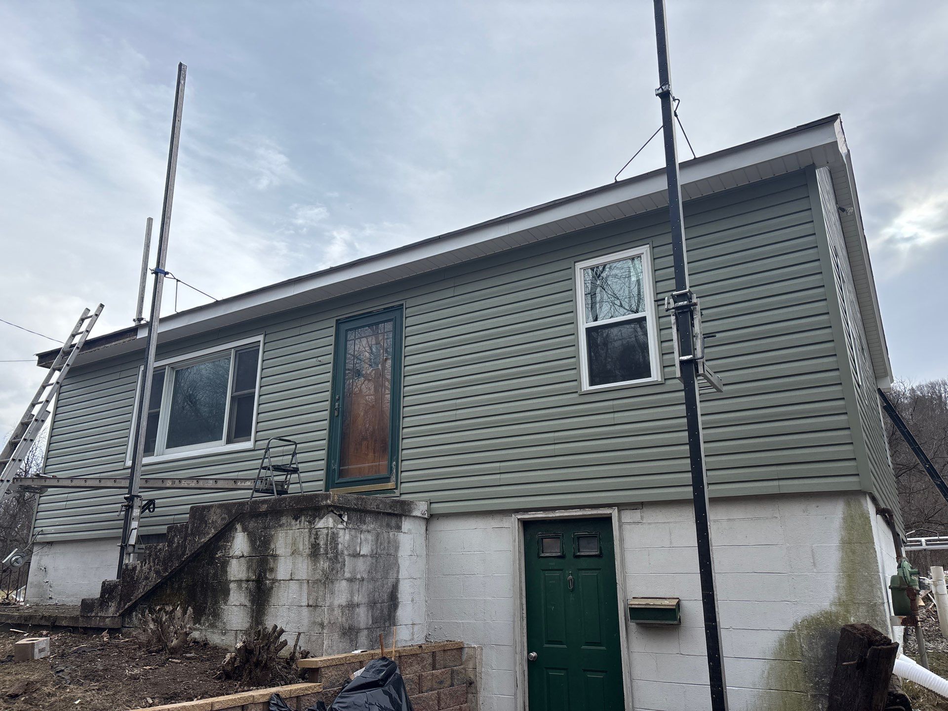 Home exterior featuring newly installed vinyl siding, scaffolding for installation, and a green door, showcasing Alan Construction's professional siding service in Pittsburgh.