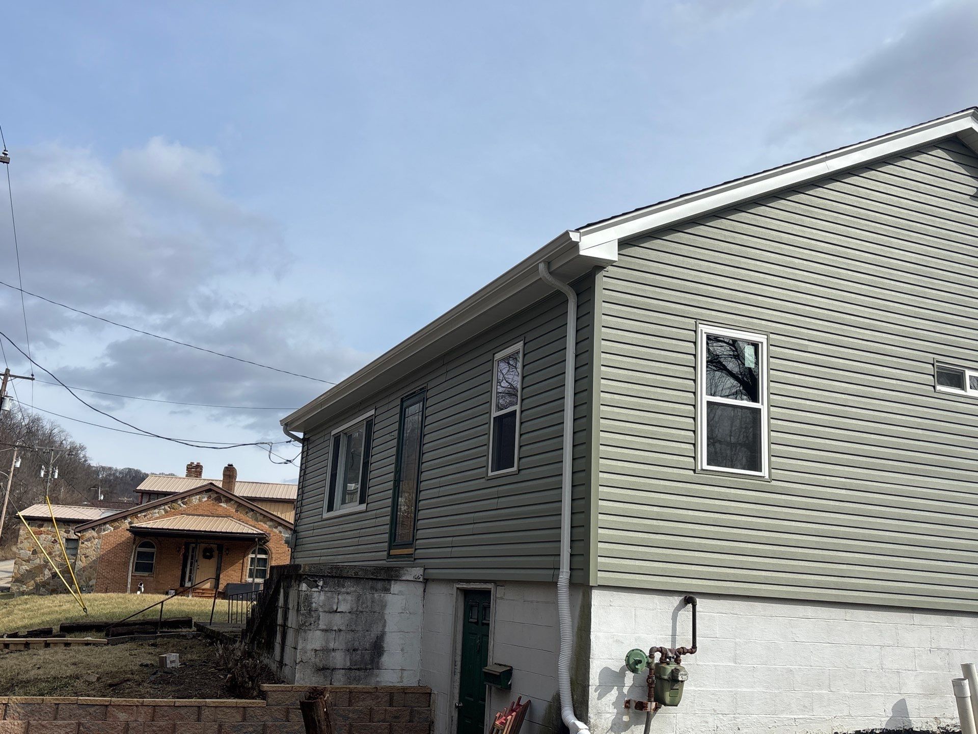Home exterior featuring newly installed green vinyl siding, showcasing enhanced aesthetic appeal and protection, with adjacent structures visible in the background.
