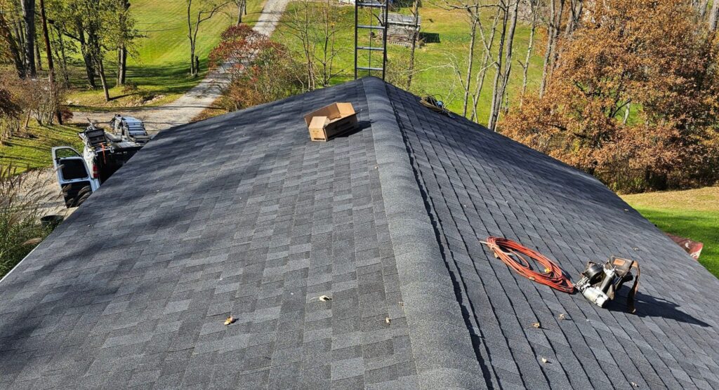 Newly installed asphalt shingle roof with tools and equipment on the surface, surrounded by trees and a clear pathway in the Pittsburgh area, showcasing quality roofing services by Alan Construction.