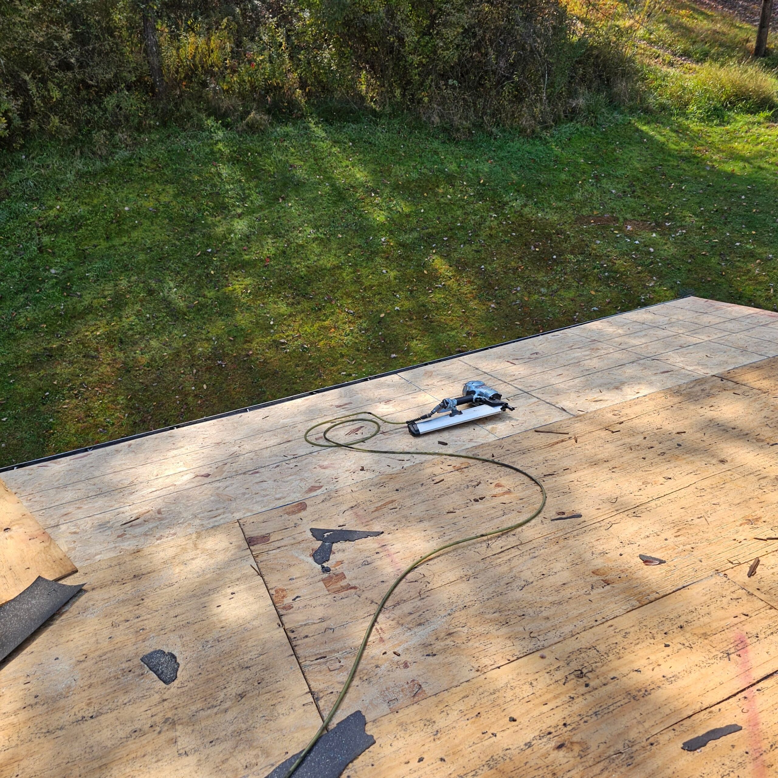 Roofing project in progress showing exposed plywood deck with a nail gun and power cord, highlighting the preparation for new roof installation in Natrona Heights.