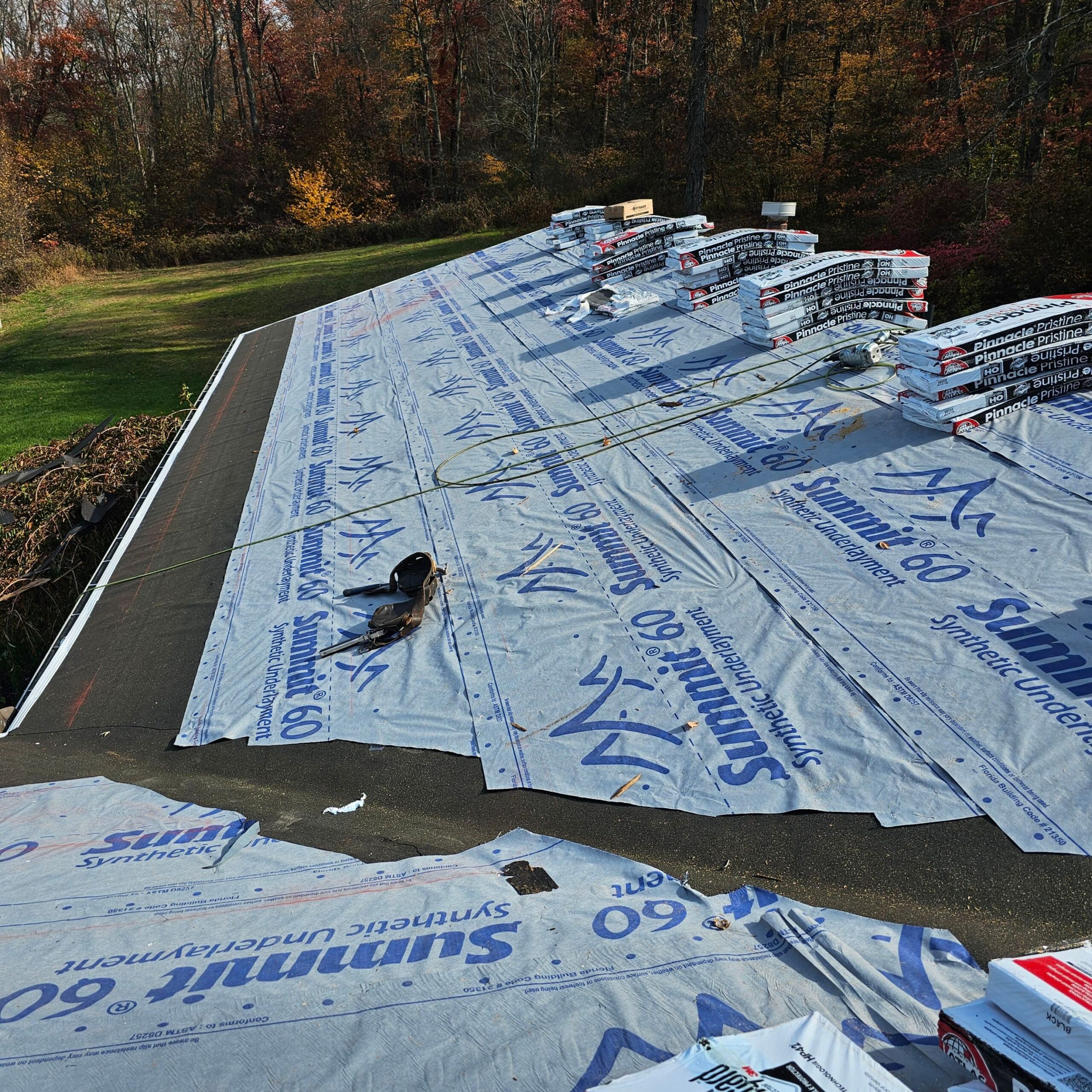 Roof underlayment installation with Summit 60 synthetic underlayment and roofing shingles stacked for residential roof replacement in Pittsburgh.