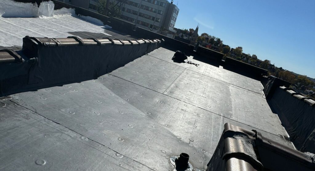 Rubber roof installation showing smooth, black surface with edge detail and clear sky, representing quality roofing services by Alan Construction in Pittsburgh.