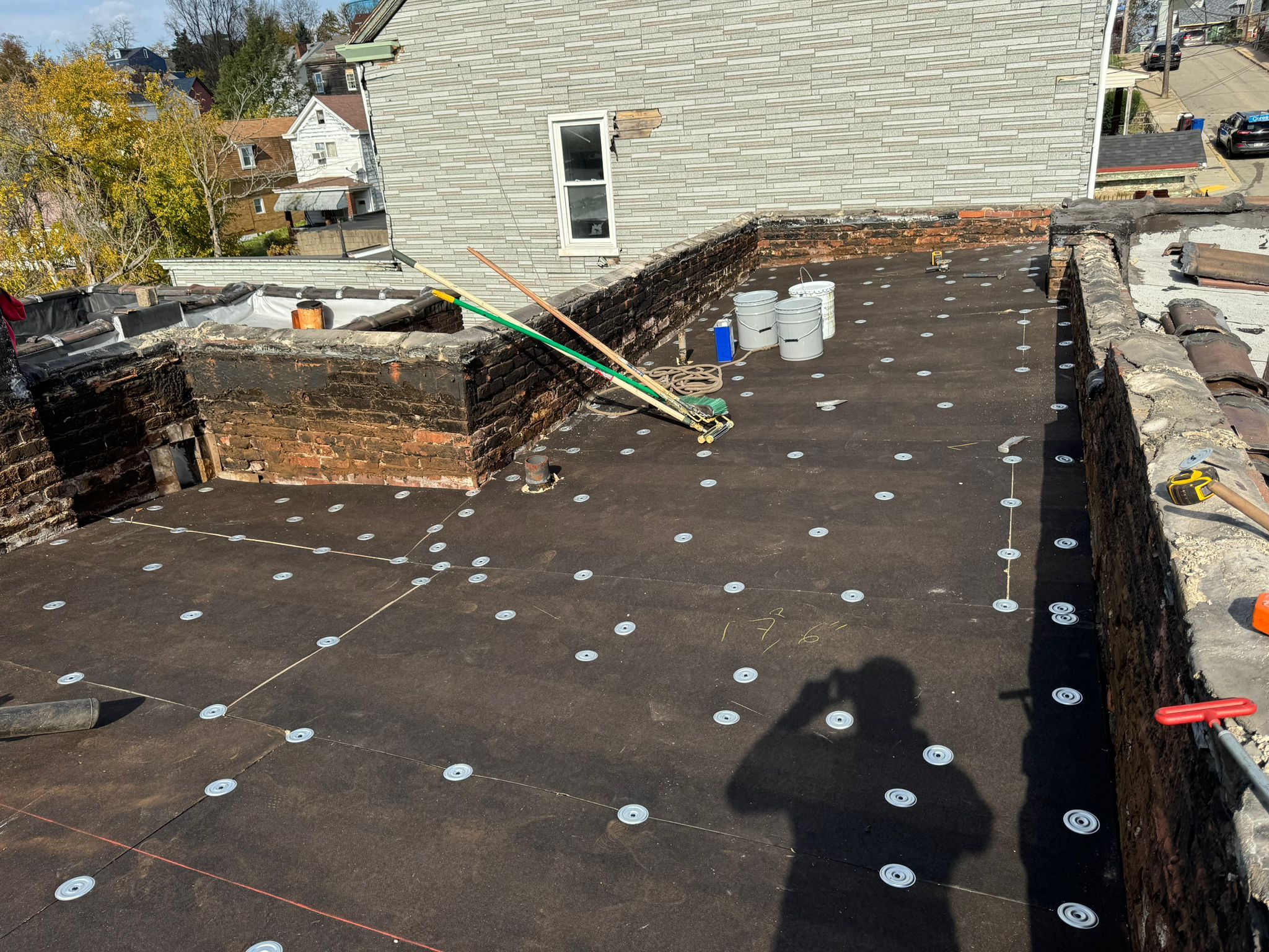 Rubber roof installation in progress on a South Side property, featuring a flat roof deck with fiber board and securing plates, surrounded by construction tools and materials.