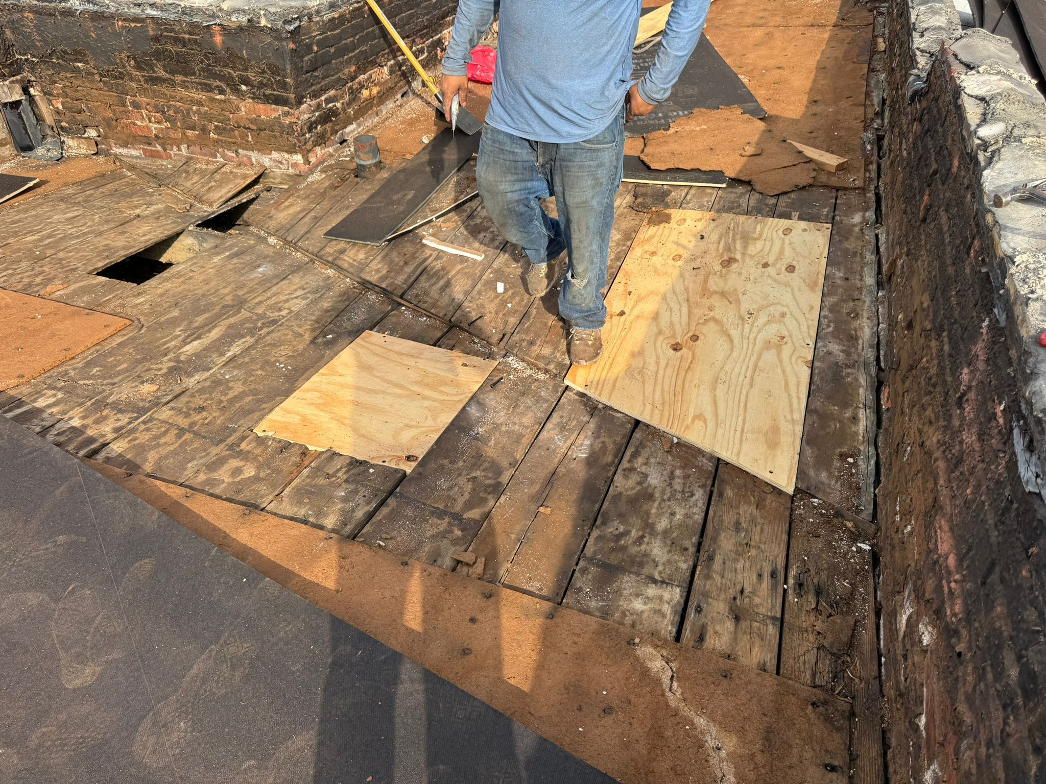 Worker installing plywood on a flat roof deck during rubber roof replacement, with visible areas of inspection and preparation for EPDM rubber roofing in South Side, Pittsburgh.