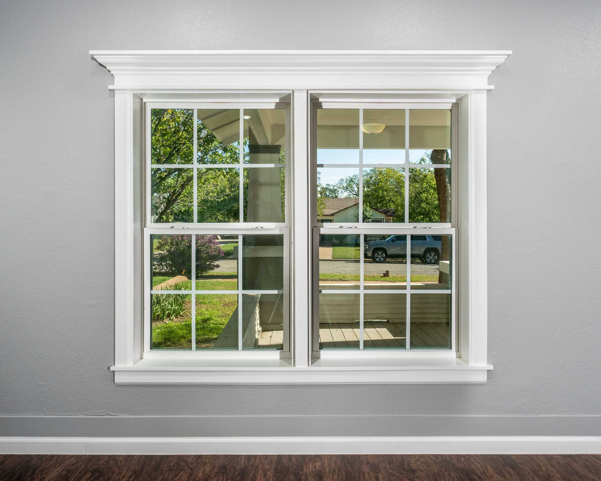 Interior view of a double-hung window with white trim, showcasing a clear view of a green landscape and residential area, emphasizing energy-efficient window replacement services offered by Alan Construction in Pittsburgh.