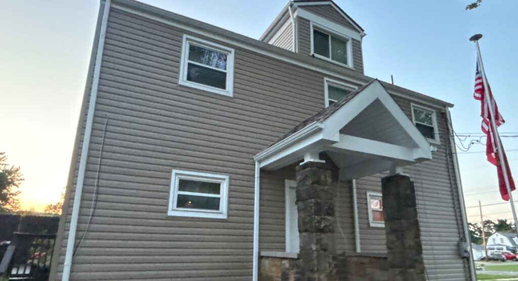 Siding replacement on a residential building showcasing new, light-colored vinyl siding with white trim and a stone entryway, emphasizing quality craftsmanship by Alan Construction in Pittsburgh.