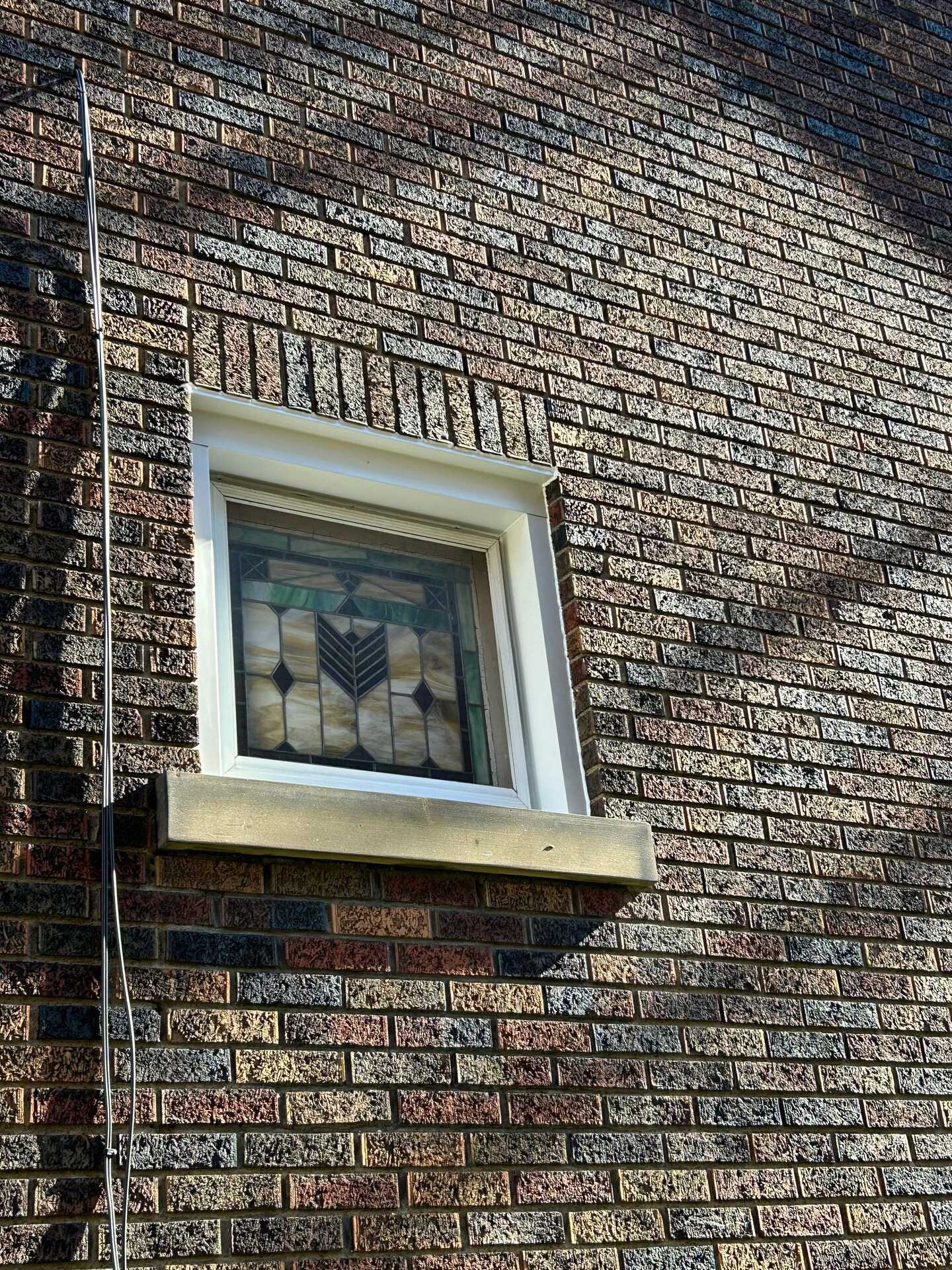 Window with decorative stained glass set in brick exterior, showcasing window flashing repair by Alan Construction in Perry North.
