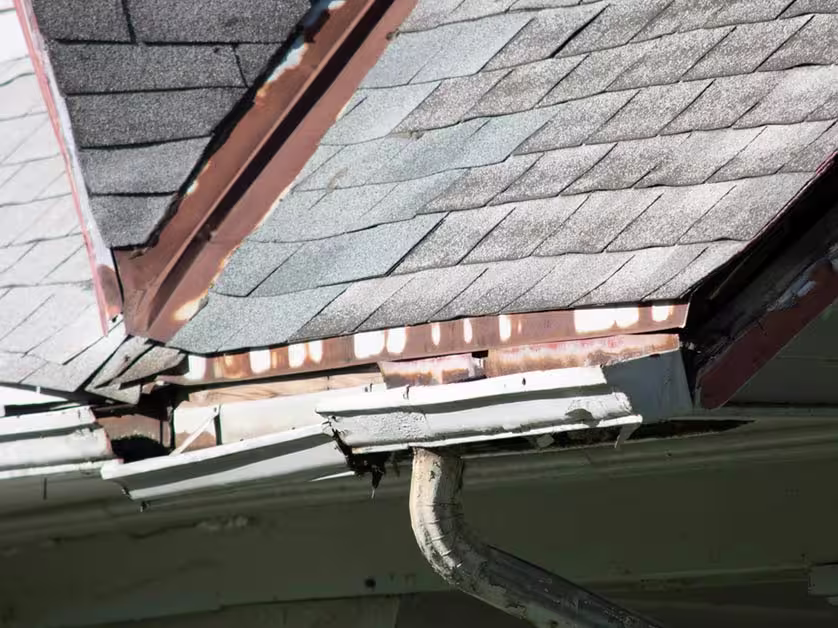 Damaged gutter section pulling away from the roofline near asphalt shingles.