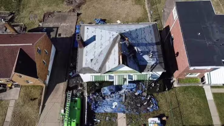 Aerial view of a residential home with roof damage and tarps covering the property.
