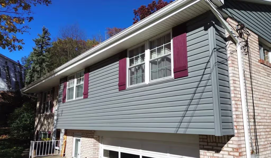 Gray vinyl siding installation on a home with white windows and red shutters.