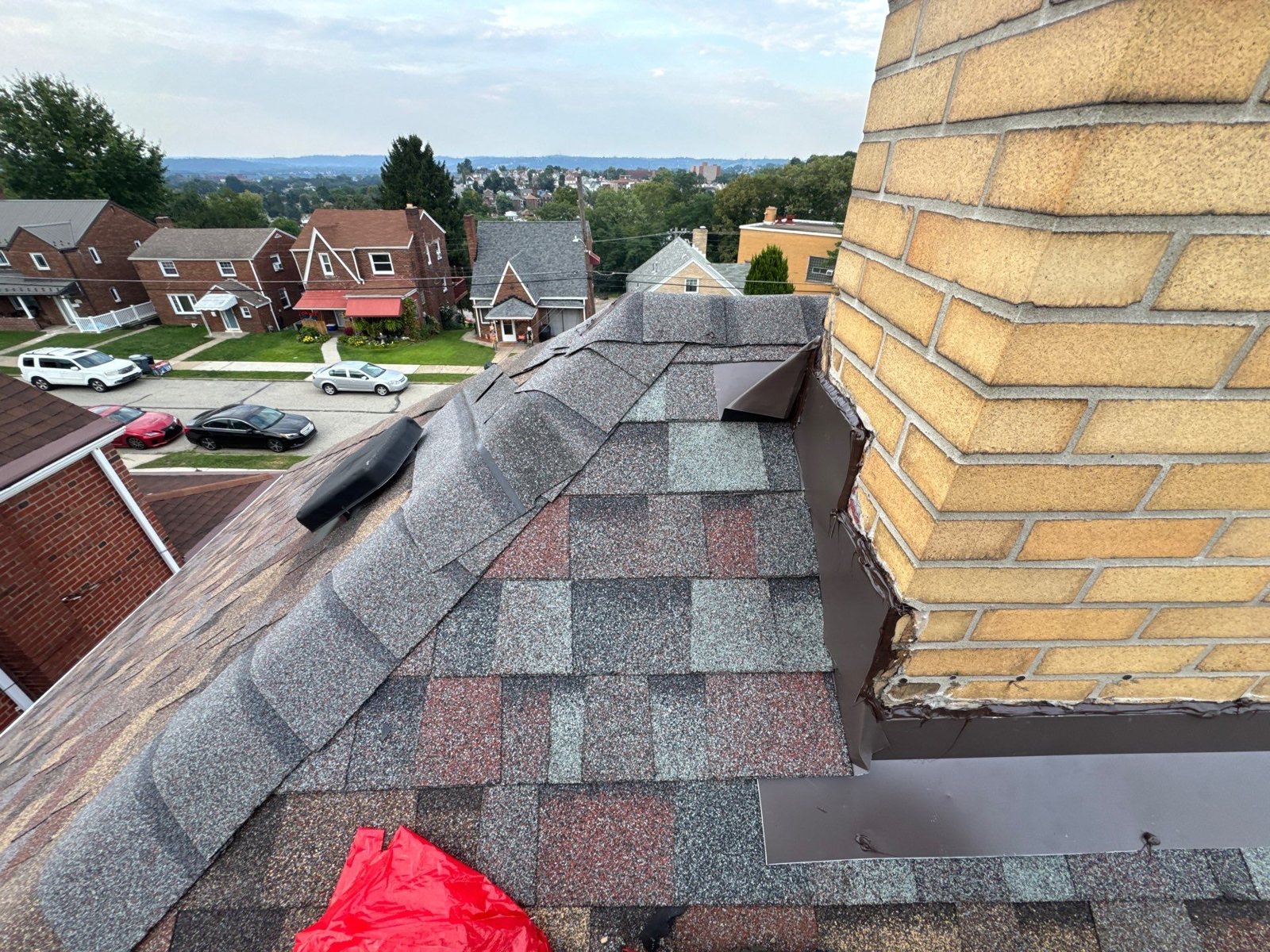 Brown metal flashing along a yellow brick chimney on multicolor shingles in Munhall, Alan Construction