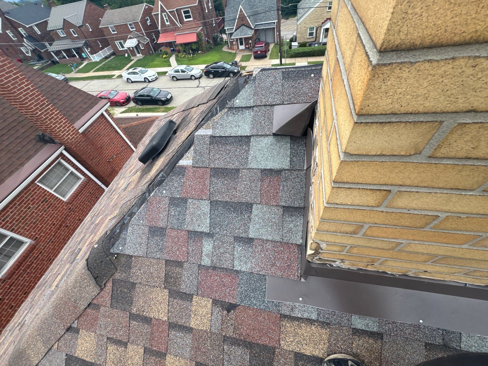 Brown metal flashing along a yellow brick chimney on multicolor shingles in Munhall, Alan Construction