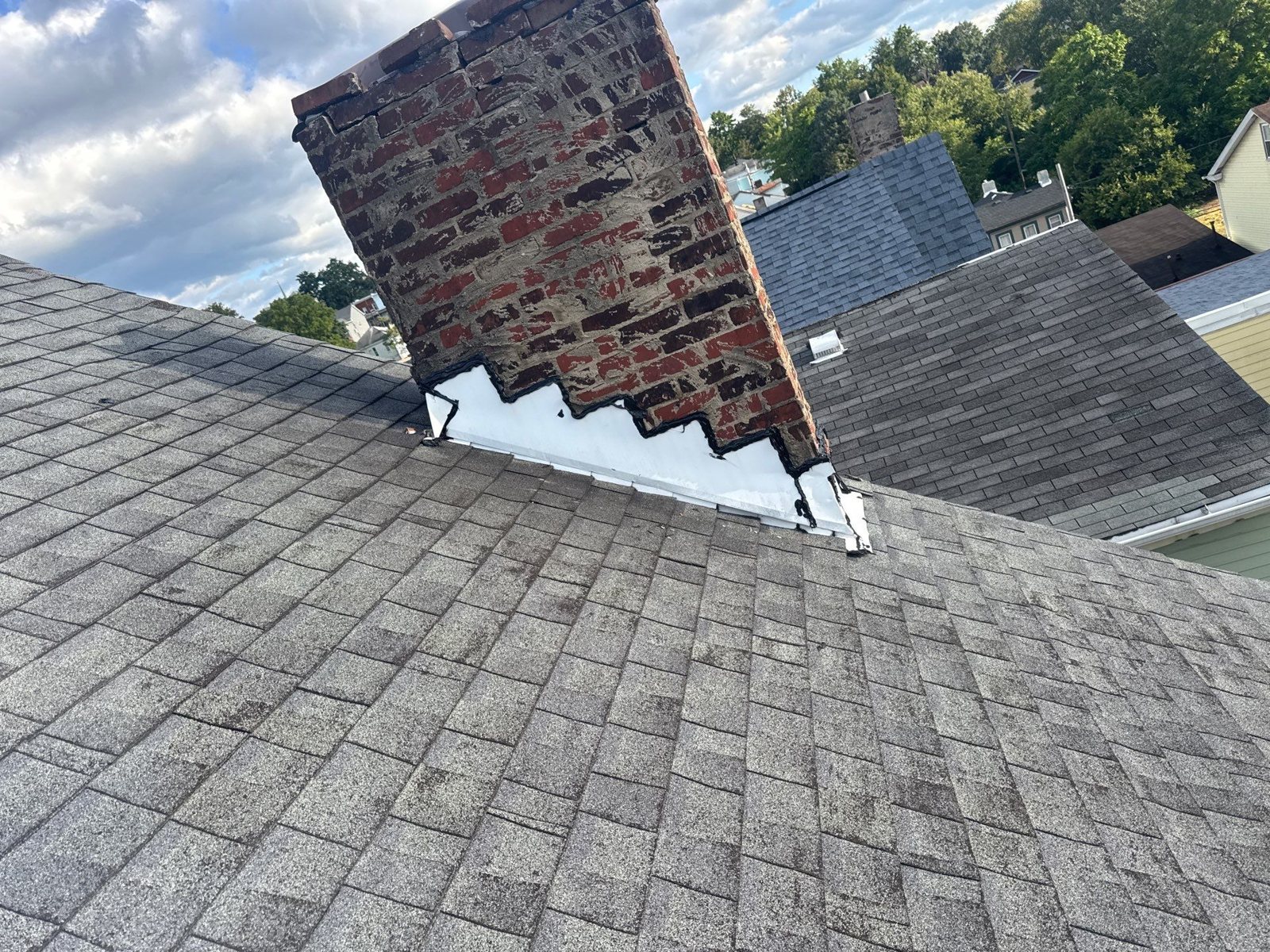 White step flashing along a red brick chimney on a gray shingle roof in Pittsburgh, Alan Construction