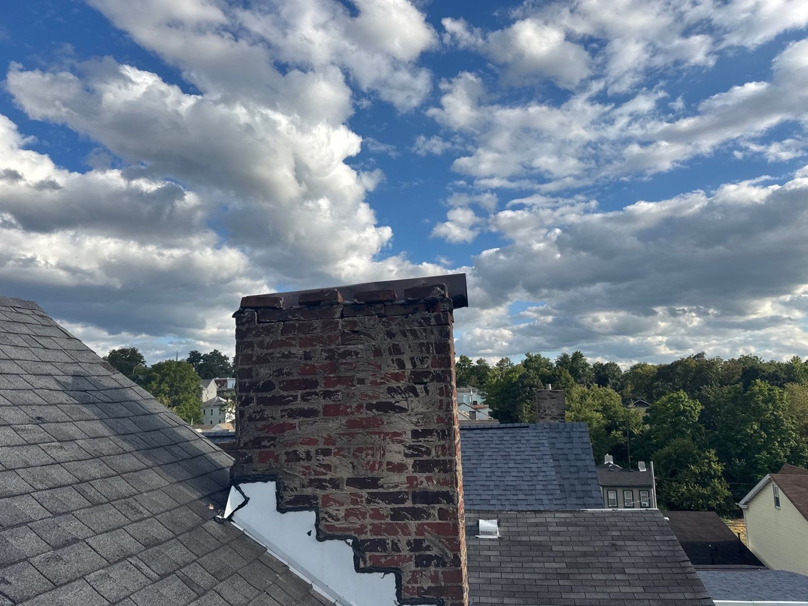 Red brick chimney with new white step flashing under a cloudy sky in Pittsburgh, Alan Construction