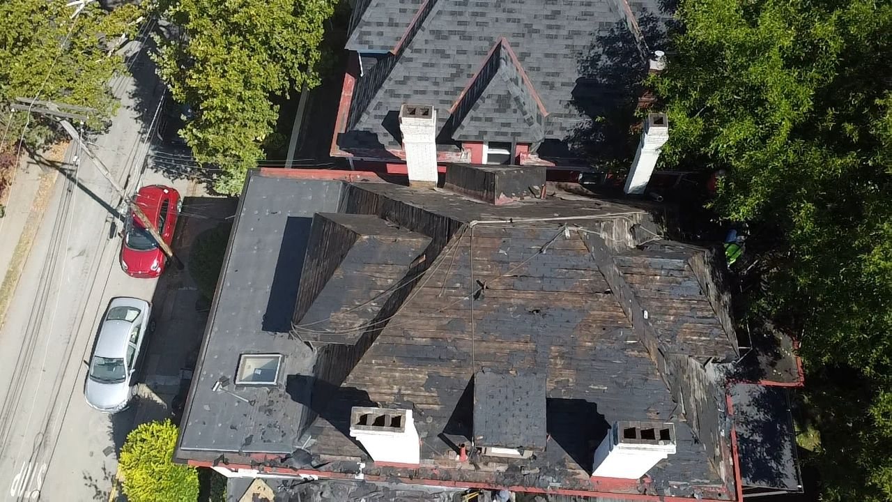 Drone view of a worn dark roof with skylights and chimneys in Pittsburgh, Alan Construction