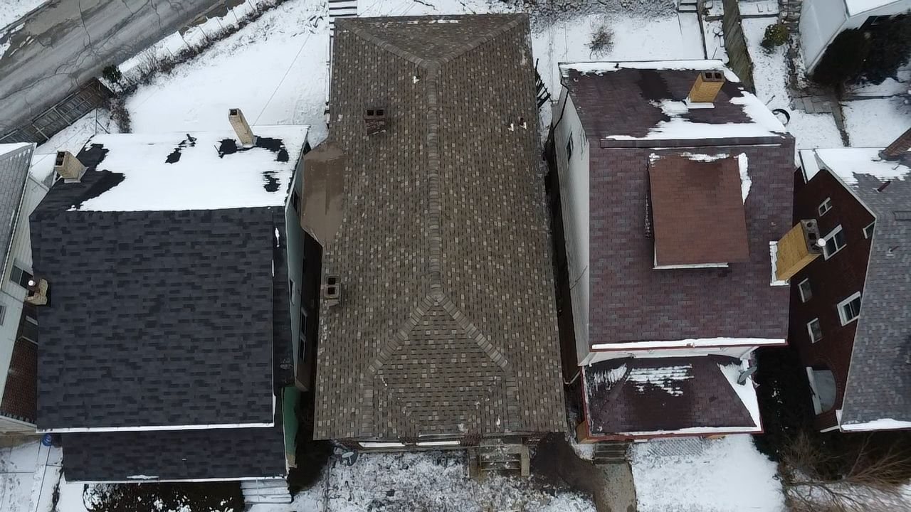Drone view of a worn shingle roof between snowy neighboring houses in Pittsburgh, Alan Construction