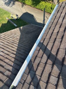 New white gutter with guard running along a shingle roof edge in Carnegie, Alan Construction