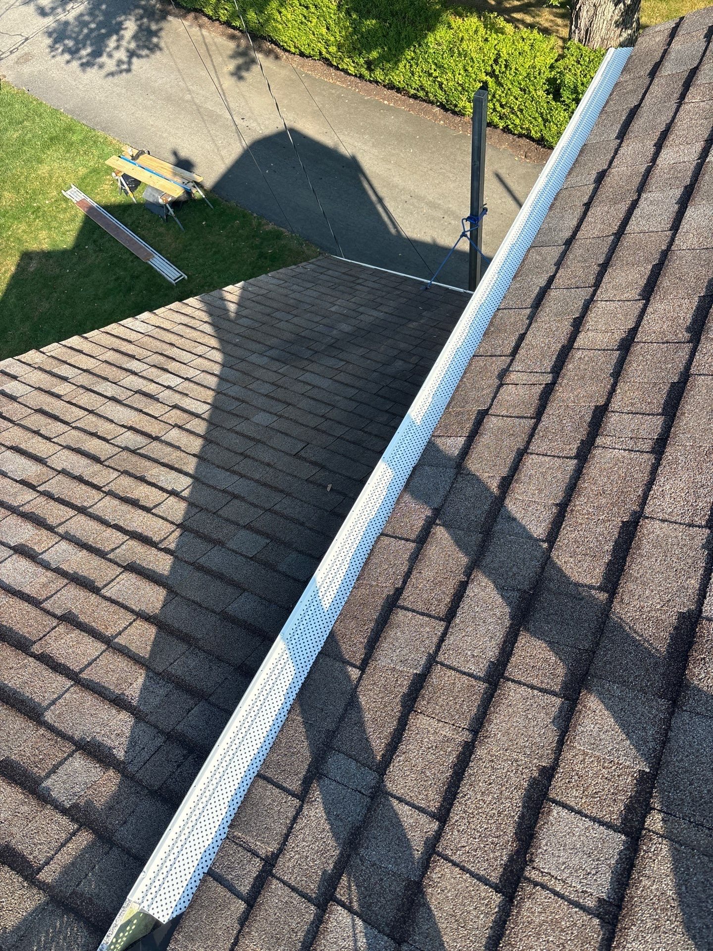 New white gutter with guard running along a shingle roof edge in Carnegie, Alan Construction