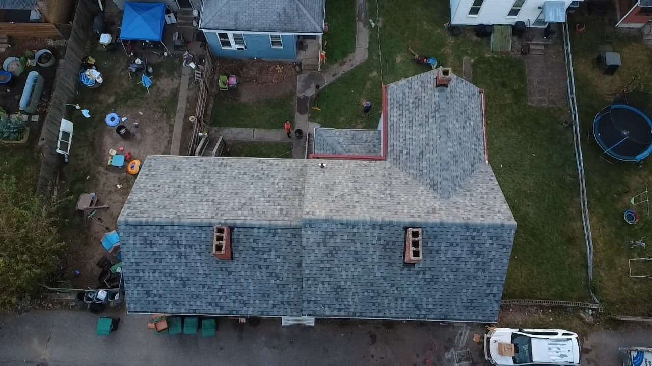 Drone view of a finished gray shingle roof with brick chimneys in Glassport, Alan Construction