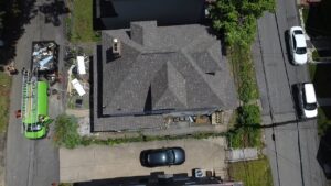 Drone view of a gray shingle roof with a green dumpster in the driveway in Pittsburgh, Alan Construction