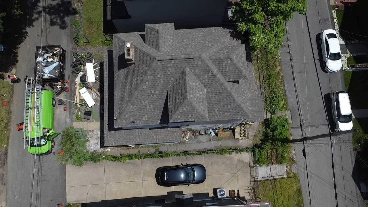 Drone view of a gray shingle roof with a green dumpster in the driveway in Pittsburgh, Alan Construction