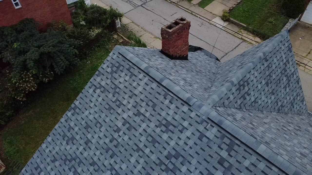 Close aerial view of new gray architectural shingles around a brick chimney in Pittsburgh, Alan Construction