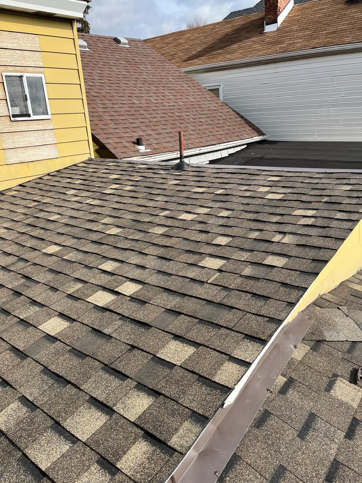 New brown shingles beside yellow siding and a neighboring roof in Pittsburgh, Alan Construction