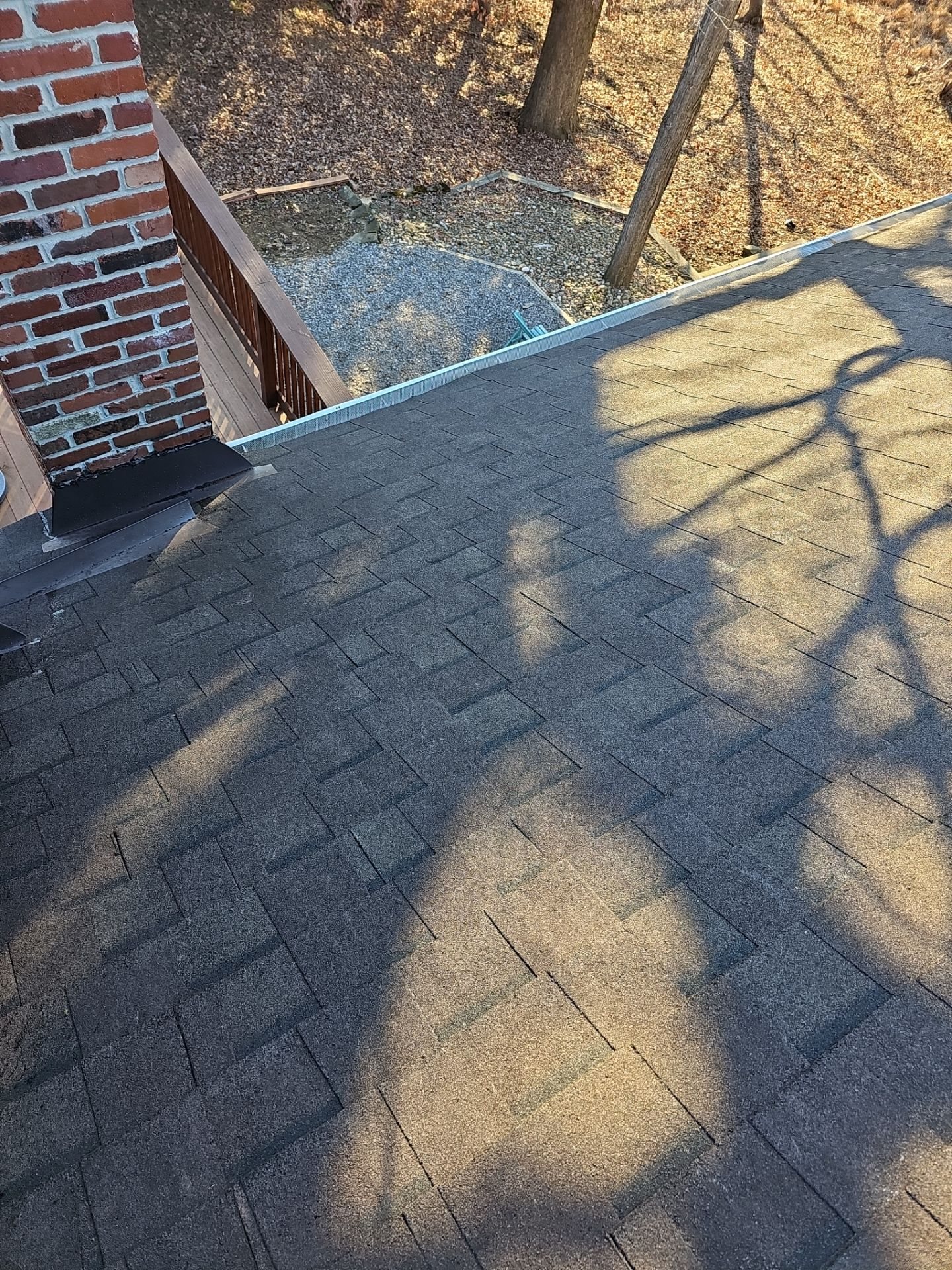 New shingles meeting a brick chimney with tree shadows in Pittsburgh, Alan Construction