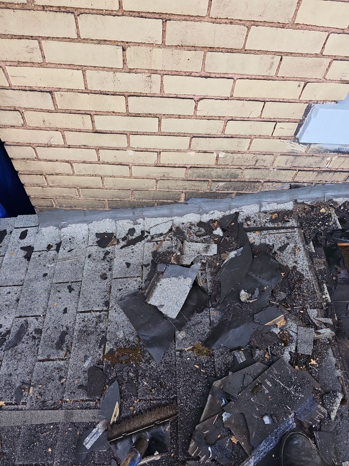Old shingle debris on a stripped roof against a brick wall in McKeesport, Alan Construction