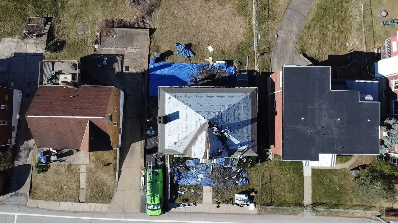 Overhead drone view of a hip roof during tearoff with tarps and dumpster in Pittsburgh, Alan Construction