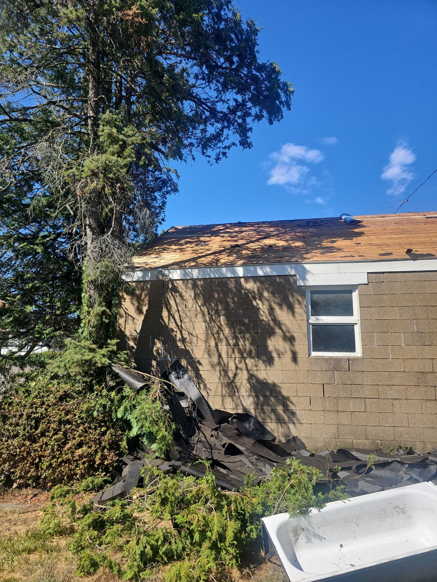 Tearoff debris piled beside a brick house with partly stripped roof in Pittsburgh, Alan Construction