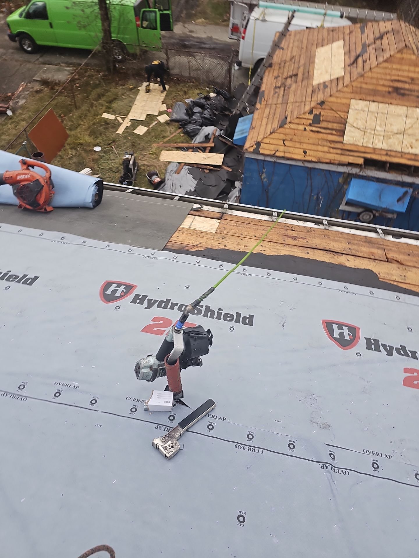 Synthetic underlayment with a nail gun on top beside a stripped roof in Clairton, Alan Construction