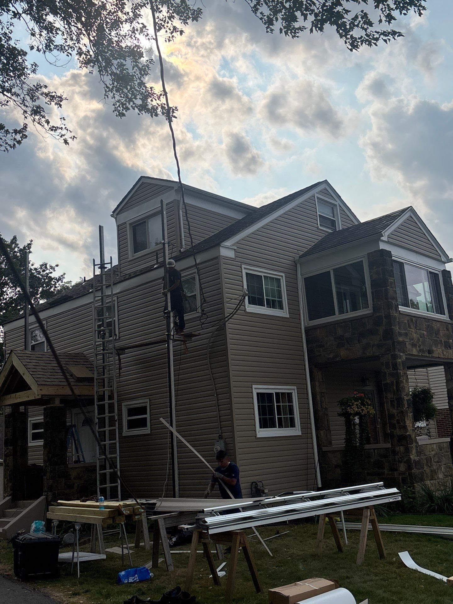 Siding crew setup with ladders and sawhorses beside a house in Carnegie, Alan Construction