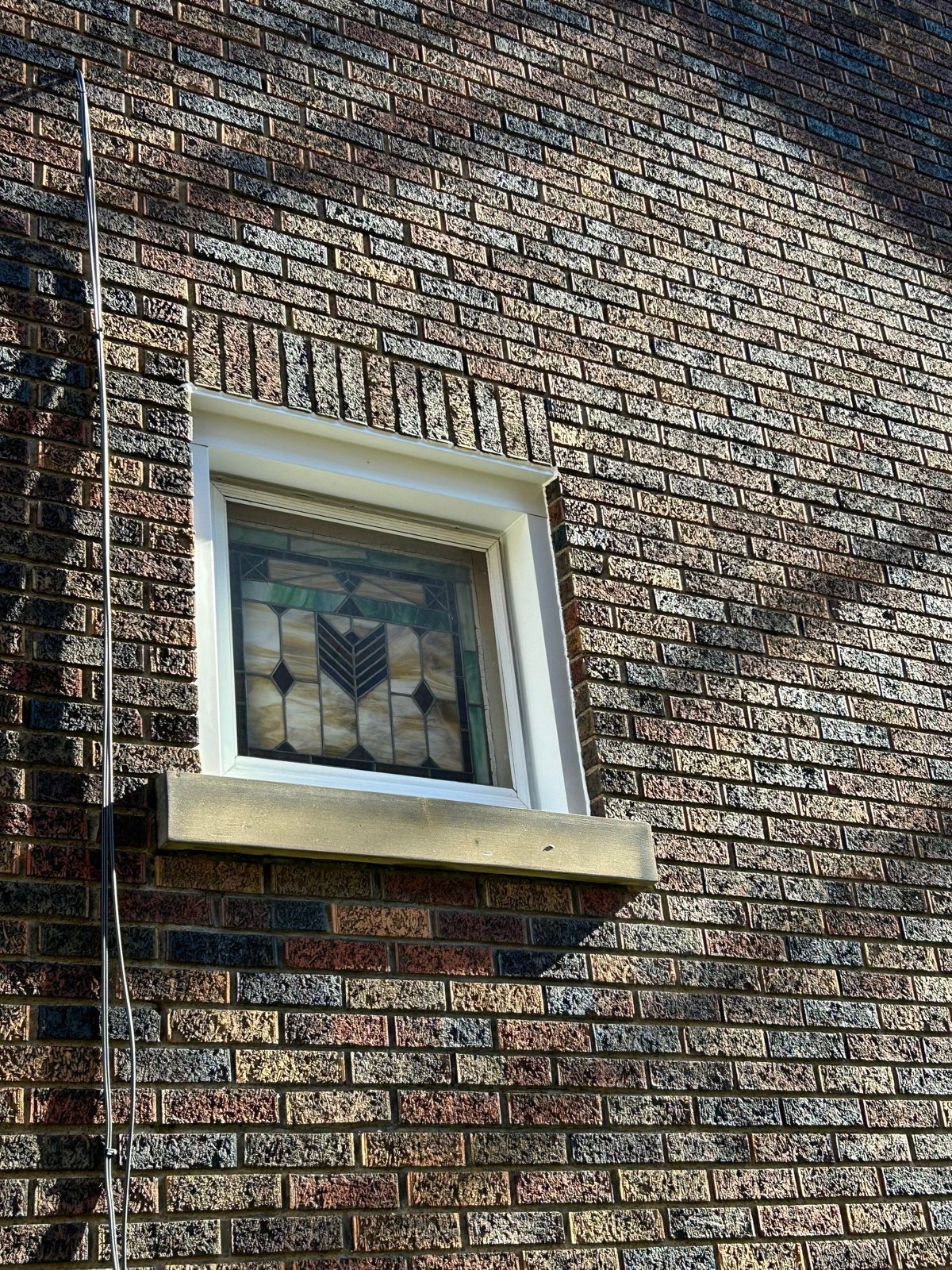 Stained glass window with a stone sill set in a brick wall in Pittsburgh, Alan Construction