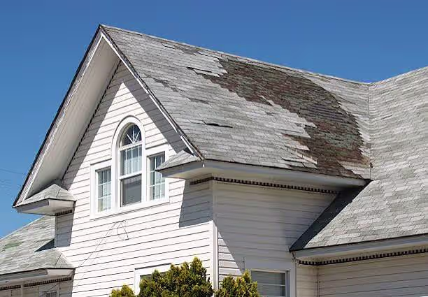 Missing shingles on a two-story home's roof after a windstorm, with the underlayment showing