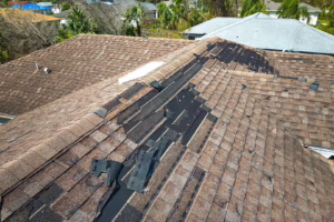 Roof wind damage with torn and missing asphalt shingles along a ridge, exposing dark underlayment